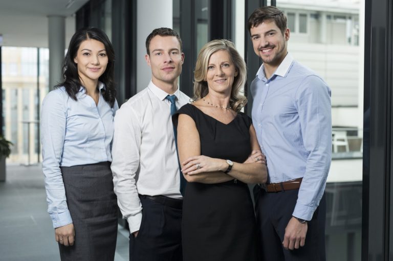Four professionals in office environment posing together.